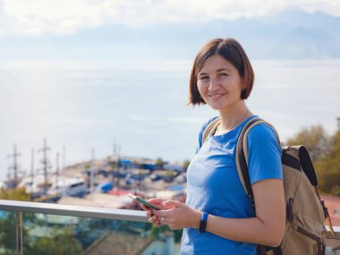 Türkiye 'ye, eski Antalya Kaleci' ye. Eski şehirde sırt çantalı mutlu Asyalı turist kadın yürüyüşçüler. Eski kasabayı ve limanı gözetleyen bir kadın var. Elinde cep telefonu var..