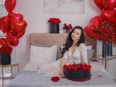 Beyaz elbiseli genç bir kadın yatakta oturuyor. Sabah aşkı yatak odası. Yıldönümü, mutlu yıllar, düğün, aşk günü, kadınlar günü, sevgililer günü ve olumlu duygular.