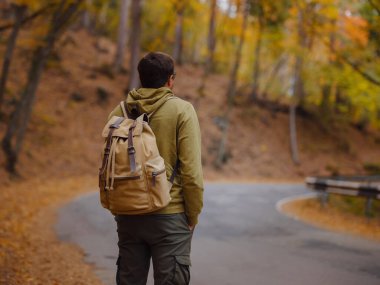 Young handsome man posing in autumn forest on road. young hipster guy with backpack , traveller standing in woods, Hiking, Forest, Journey, active healthy lifestyle, adventure, vacation concept.