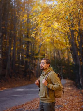 Young handsome man posing in autumn forest. young hipster guy with backpack , traveller standing in woods, Hiking, Forest, Journey, active healthy lifestyle, adventure, vacation concept.