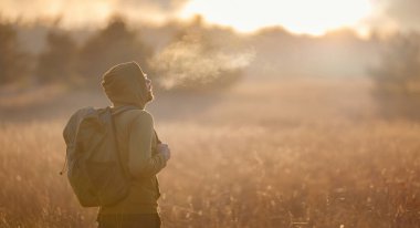 Sonbahar doğasında poz veren genç yakışıklı bir adam. Adam gün batımında sahada duruyor. Hedefler, umutlar ve özlemler konsepti. Doğa manzarasının tadını. Yürüyüş ve yürüyüş. Konsept Macera ve Seyahat
