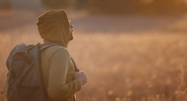 Young handsome man posing in autumn nature. guy standing in field over sunset. Goals, hopes and aspirations concept. enjoying nature view. Hiking and trekking. Concept Adventure and Travel