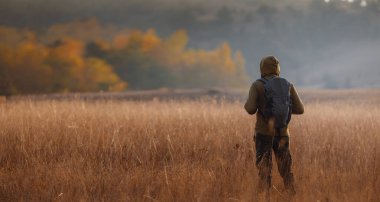 Sonbahar doğasında poz veren genç yakışıklı bir adam. Adam gün batımında sahada duruyor. Hedefler, umutlar ve özlemler konsepti. Doğa manzarasının tadını. Yürüyüş ve yürüyüş. Konsept Macera ve Seyahat