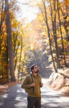 Young handsome man posing in autumn forest. young hipster guy with backpack , traveller standing in woods, Hiking, Forest, Journey, active healthy lifestyle, adventure, vacation concept.