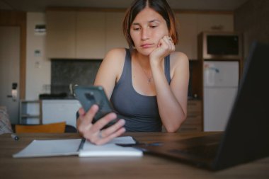 Evdeki genç Asyalı kadın, uzaktan kumandalı. Ondan güzel bir mesaj. Çekici genç bayan akıllı telefonuna bakıyor ve oturma odasında otururken gülümsüyor..