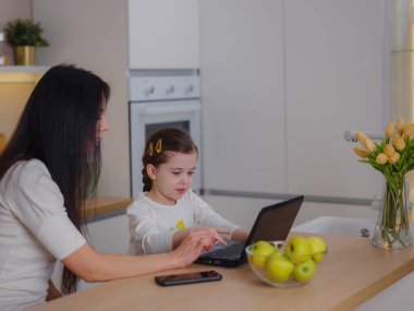 Çalışan anne ev ofisinde çalışıyor. Kadın ve çocuk dizüstü bilgisayar kullanıyor. Rahat bir mutfakta serbest çalışanların işyeri. Kadın işi, nezaket, ilgi. Yaşam biçimi.