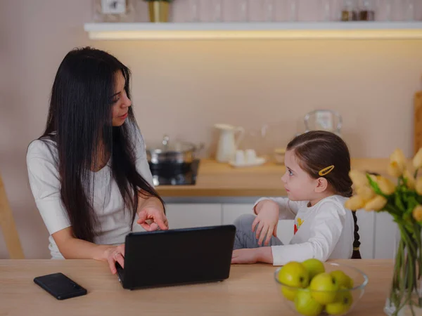 working mom works from home office. woman and child using laptop. Freelancers workplace in cozy kitchen. Womens business, kindness, care. Lifestyle.