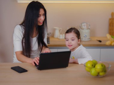 Çalışan anne ev ofisinde çalışıyor. Kadın ve çocuk dizüstü bilgisayar kullanıyor. Rahat bir mutfakta serbest çalışanların işyeri. Kadın işi, nezaket, ilgi. Yaşam biçimi.