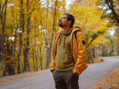 Young handsome man posing in autumn forest. young hipster guy with backpack , traveller standing in woods, Hiking, Forest, Journey, active healthy lifestyle, adventure, vacation concept.