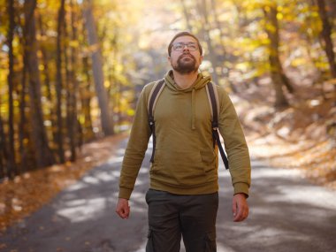 Young handsome man posing in autumn forest. young hipster guy with backpack , traveller standing in woods, Hiking, Forest, Journey, active healthy lifestyle, adventure, vacation concept.