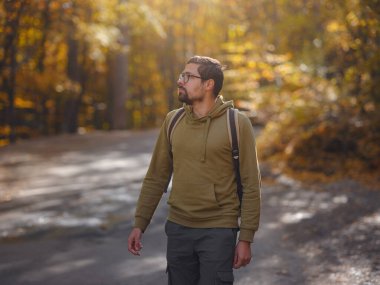 Young handsome man posing in autumn forest. young hipster guy with backpack , traveller standing in woods, Hiking, Forest, Journey, active healthy lifestyle, adventure, vacation concept.