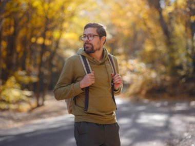 Young handsome man posing in autumn forest. young hipster guy with backpack , traveller standing in woods, Hiking, Forest, Journey, active healthy lifestyle, adventure, vacation concept.