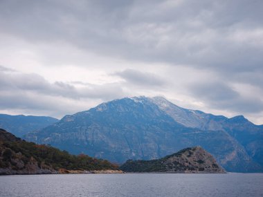 Oludeniz, Fethiye, Türkiye 'deki Lagün' e git. Darbogaz yakınlarında bir plaj. Babadag Dağı manzaralı, dağlı kış manzaralı, yeşil orman, masmavi su, plaj ve bulutlu gökyüzü