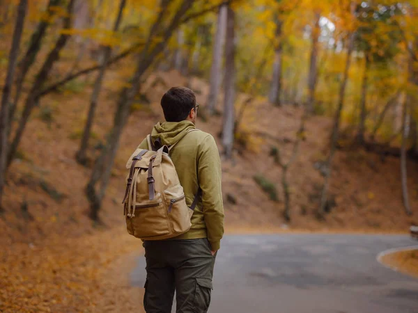 Young handsome man posing in autumn forest on road. young hipster guy with backpack , traveller standing in woods, Hiking, Forest, Journey, active healthy lifestyle, adventure, vacation concept.
