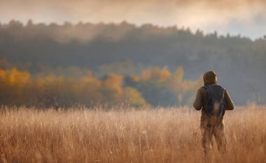 Sonbahar doğasında poz veren genç yakışıklı bir adam. Adam gün batımında sahada duruyor. Hedefler, umutlar ve özlemler konsepti. Doğa manzarasının tadını. Yürüyüş ve yürüyüş. Konsept Macera ve Seyahat