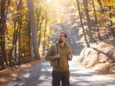 Young handsome man posing in autumn forest. young hipster guy with backpack , traveller standing in woods, Hiking, Forest, Journey, active healthy lifestyle, adventure, vacation concept.