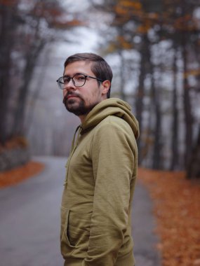 Genç yakışıklı adam sonbahar ormanlarında yolda poz veriyor. Sırt çantalı genç hippi, ormanda duran gezgin, yürüyüş, orman, yolculuk, aktif sağlıklı yaşam tarzı, macera, tatil konsepti..