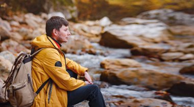 Sonbaharda seyahat ve yolculuk konsepti. Macera ve aktif yaşam tarzı. Ormanda turist yürüyüşü. Sarı ceketli beyaz adam ormanda yürüyor..