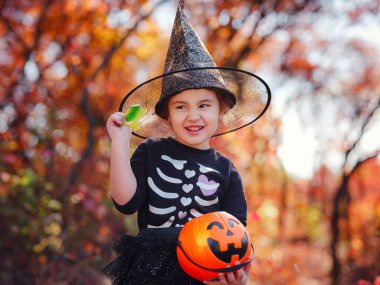 Young girl in black costume goes trick or treating. Little witch, Kids with jack-o-lantern. Children with candy bucket in fall forest. Happy Halloween.