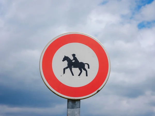 Prohibition sign for horses and riders. Triangular sign with red stripe and dark image on light background of rider on horse.