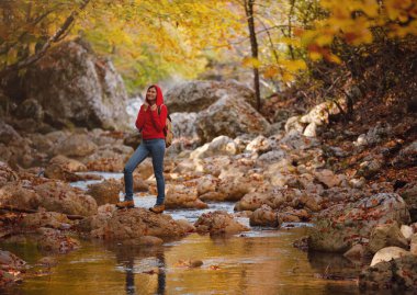 Sonbaharda seyahat ve yolculuk konsepti. Macera ve aktif yaşam tarzı. Ormanda turist yürüyüşü. Kırmızı kapüşonlu Asyalı kadın ormanda yürüyor. Seyahat tutkusu konsepti.