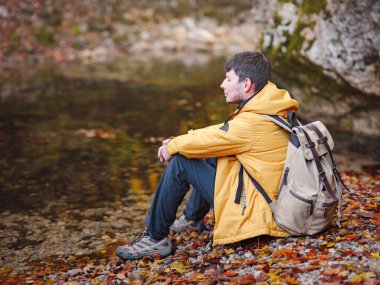 Sonbaharda seyahat ve yolculuk konsepti. Macera ve aktif yaşam tarzı. Ormanda turist yürüyüşü. Sarı ceketli beyaz adam ormanda yürüyor..