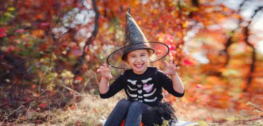 Young girl in black costume goes trick or treating. Little witch, Kids with jack-o-lantern. Children with candy bucket in fall forest. Happy Halloween.