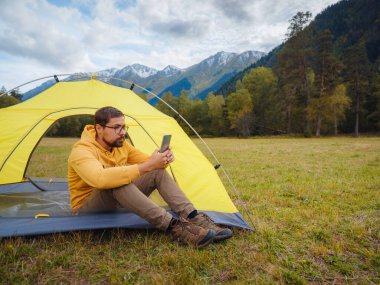 trip to Caucasus mountains, Arkhyz, Teberdinsky reserve. Man traveler relaxing in mountains in tent camping outdoor , uses app on smartphone. Travel adventure lifestyle concept hiking active vacations