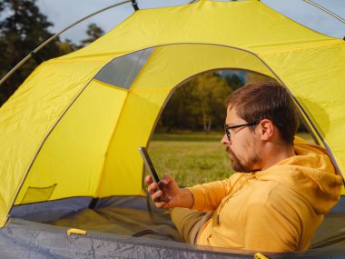 trip to Caucasus mountains, Arkhyz, Teberdinsky reserve. Man traveler relaxing in mountains in tent camping outdoor , uses app on smartphone. Travel adventure lifestyle concept hiking active vacations
