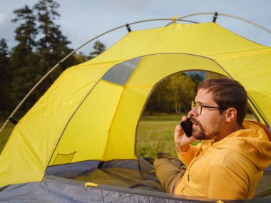 trip to Caucasus mountains, Arkhyz, Teberdinsky reserve. Man traveler relaxing in mountains in tent camping outdoor , uses app on smartphone. Travel adventure lifestyle concept hiking active vacations