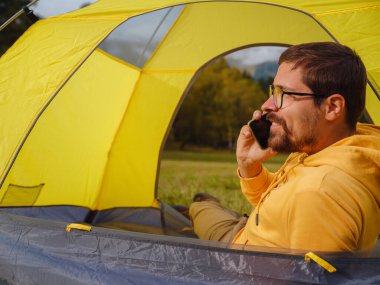 trip to Caucasus mountains, Arkhyz, Teberdinsky reserve. Man traveler relaxing in mountains in tent camping outdoor , uses app on smartphone. Travel adventure lifestyle concept hiking active vacations