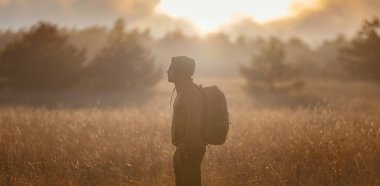 Sonbahar doğasında poz veren genç yakışıklı bir adam. Adam gün batımında sahada duruyor. Hedefler, umutlar ve özlemler konsepti. Doğa manzarasının tadını. Yürüyüş ve yürüyüş. Konsept Macera ve Seyahat