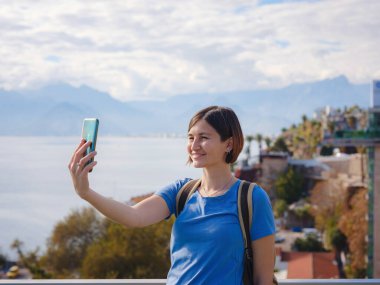 Türkiye 'ye, eski Antalya Kaleci' ye. Eski şehirde sırt çantalı mutlu Asyalı turist kadın yürüyüşçüler. Eski kasabayı gözetleyen kadın ve liman manzaralı selfie çekiyor.