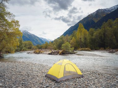 trip to Caucasus mountains, Arkhyz, Teberdinsky reserve. concept of discovery and exploration of wild places in early autumn. yellow tent on bank of mountain river