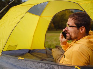 trip to Caucasus mountains, Arkhyz, Teberdinsky reserve. Man traveler relaxing in mountains in tent camping outdoor , uses app on smartphone. Travel adventure lifestyle concept hiking active vacations