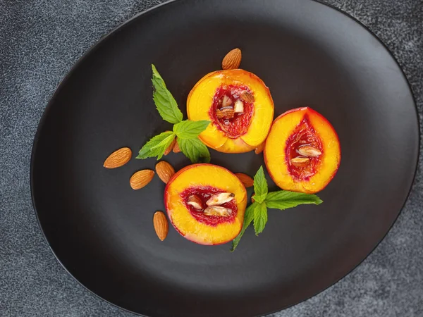Summer dessert - Cooking Ripe grilled peaches with honey and nuts over dark plate and table. Selective focus with blurred foreground and background. closeup
