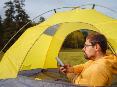 trip to Caucasus mountains, Arkhyz, Teberdinsky reserve. Man traveler relaxing in mountains in tent camping outdoor , uses app on smartphone. Travel adventure lifestyle concept hiking active vacations