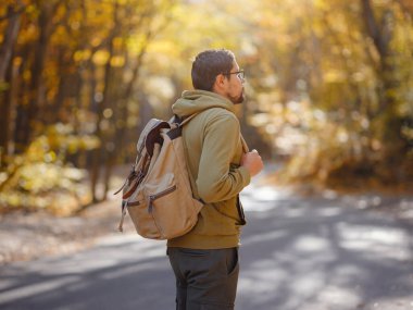 Young handsome man posing in autumn forest. young hipster guy with backpack , traveller standing in woods, Hiking, Forest, Journey, active healthy lifestyle, adventure, vacation concept.