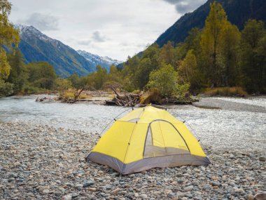 trip to Caucasus mountains, Arkhyz, Teberdinsky reserve. concept of discovery and exploration of wild places in early autumn. yellow tent on bank of mountain river