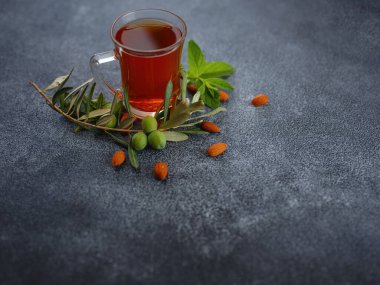 Cup of freshly brewed black tea with mint and almond nuts, warm soft light, dark background.