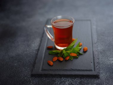 Cup of freshly brewed black tea with mint and almond nuts, warm soft light, dark background.