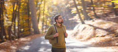 Young handsome man posing in autumn forest. young hipster guy with backpack , traveller standing in woods, Hiking, Forest, Journey, active healthy lifestyle, adventure, vacation concept.