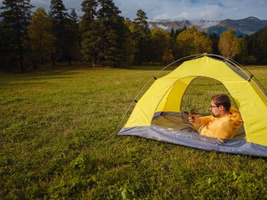 trip to Caucasus mountains, Arkhyz, Teberdinsky reserve. Man traveler relaxing in mountains in tent camping outdoor , uses app on smartphone. Travel adventure lifestyle concept hiking active vacations