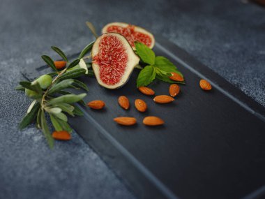 fresh ripe figs fruit almond nuts and olive branch on dark table. mediterranean food concept