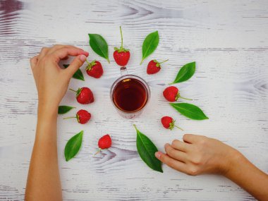 Taze organik çilekler ve cam bardakta siyah çay. Kadın eli, beyaz arka planda. Vejetaryen sağlıklı gıda konsepti.