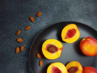 Hand holding fresh peach fruit and black dish with peaches and cloth on table blurred background. Top view. Close-up photo. Healthy food and fruit concept