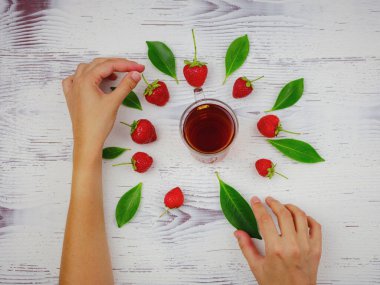 Taze organik çilekler ve cam bardakta siyah çay. Kadın eli, beyaz arka planda. Vejetaryen sağlıklı gıda konsepti.