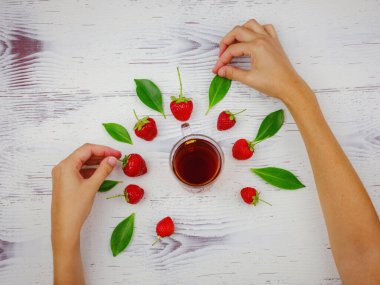 Taze organik çilekler ve cam bardakta siyah çay. Kadın eli, beyaz arka planda. Vejetaryen sağlıklı gıda konsepti.