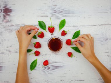 Taze organik çilekler ve cam bardakta siyah çay. Kadın eli, beyaz arka planda. Vejetaryen sağlıklı gıda konsepti.