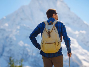Irkis Vadisi 'nden, Arkhyz' den, Karachay-Cherkessia 'dan, Kuzey Kafkasya' dan. Mavi gökyüzü, bulutlar ve Kafkasya nehri yakınlarındaki güzel ormanla karlı dağ vadisinde yürüyüş yapan bir adam..